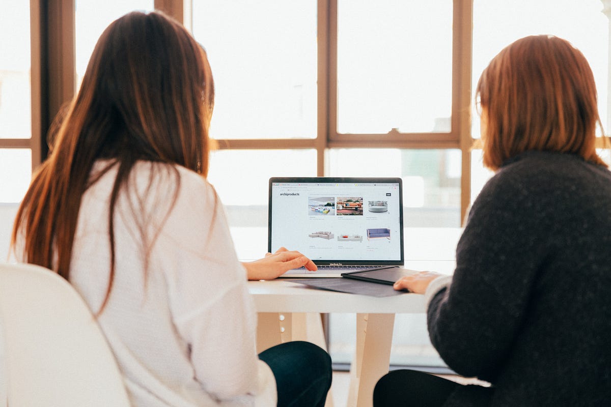 Two women looking to a couch website on a computer