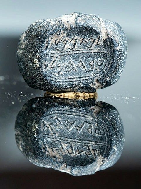 Ancient blue carved stone on a mirrored surface, pitted and sandy, with strange writing.