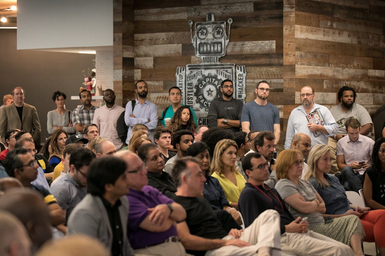 Image: A large crowd of people are standing and sitting inside while attending an event held at Capital Factory in Austin. TX.