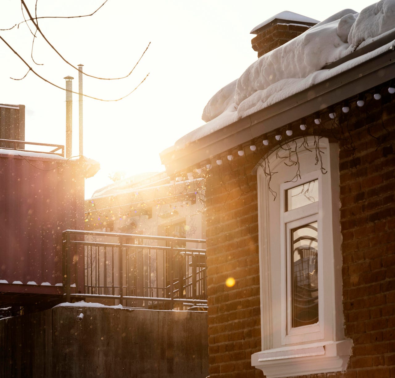 Golden sunlight streaming over a snow-covered urban landscape, highlighting the cozy charm of winter mornings. This serene scene captures the warmth and tranquility of embracing the season, even amidst the cold.