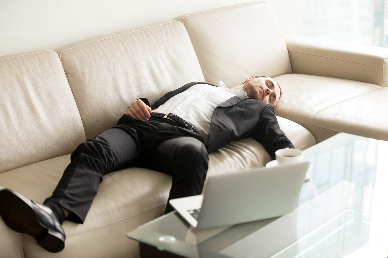 Overworked businessman in a suit asleep on a couch with a laptop and coffee nearby, emphasizing the need for balance, strategic breaks, and effective tools like timer apps to enhance productivity and well-being.