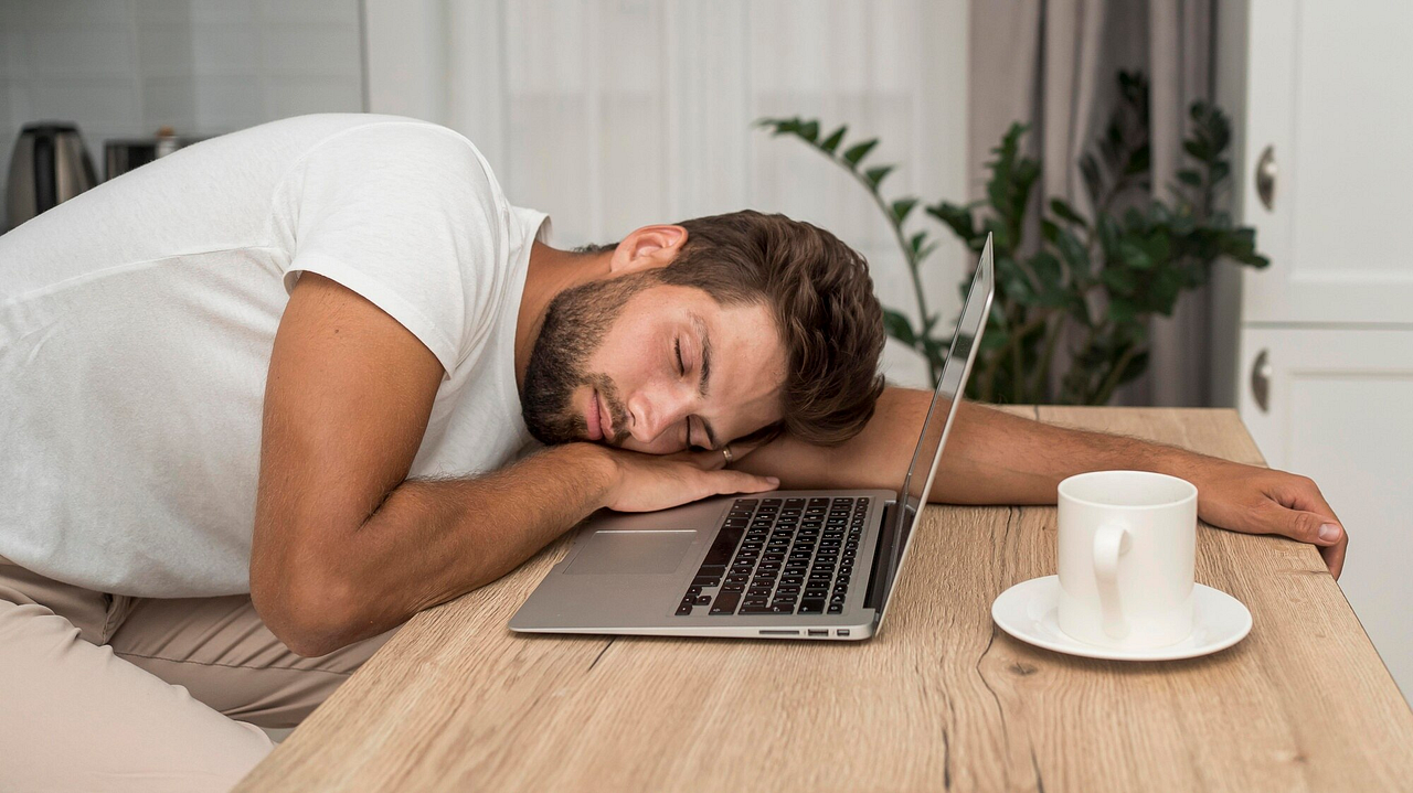 Exhausted man falls asleep on his laptop with a coffee cup nearby, highlighting the importance of breaks, proper rest, and effective tools like a timer app to manage daily productivity and avoid burnout.
