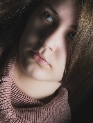 Close-up image of a young woman with brown hair, wearing a turtleneck and looking upward.