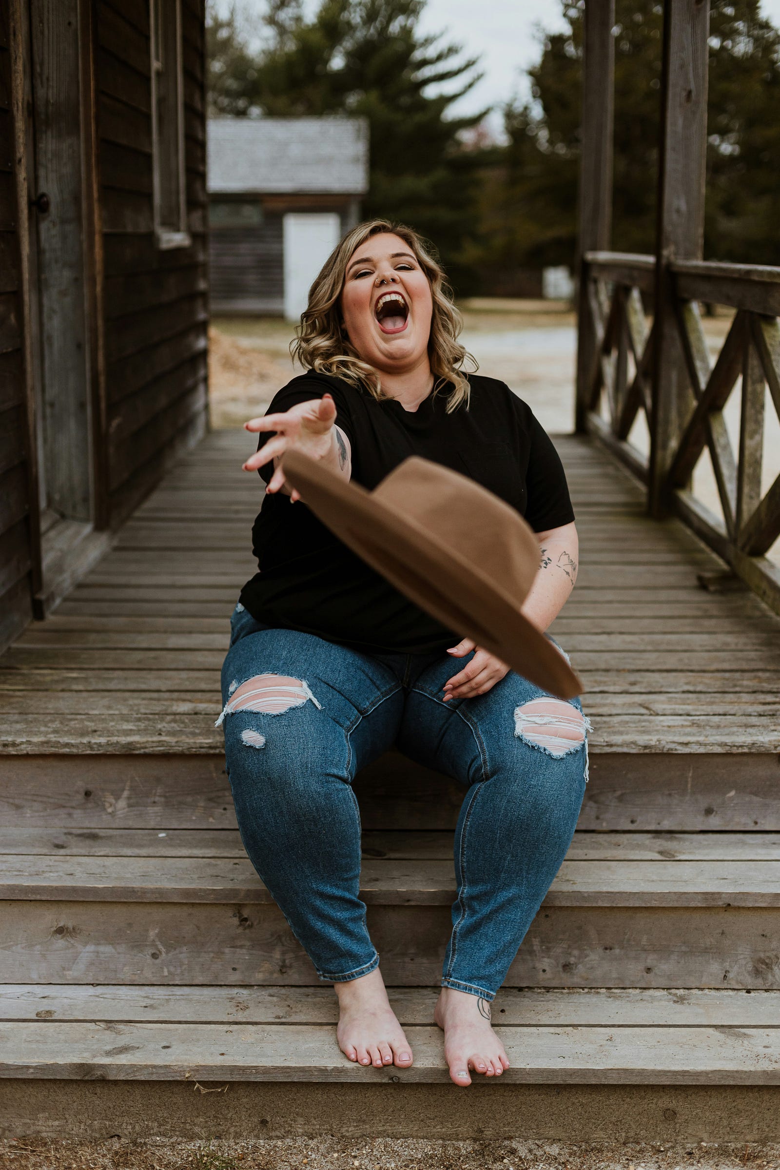 An overweight, smiling woman tosses a brown hat toward the viewer.