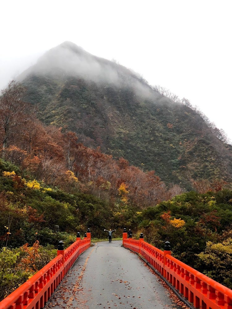 Mt. Yudono Shrine in the middle of Autumn with a peak that appears to be balding and the bright red bridge on the trail to Mt. Yudono’s object of worship