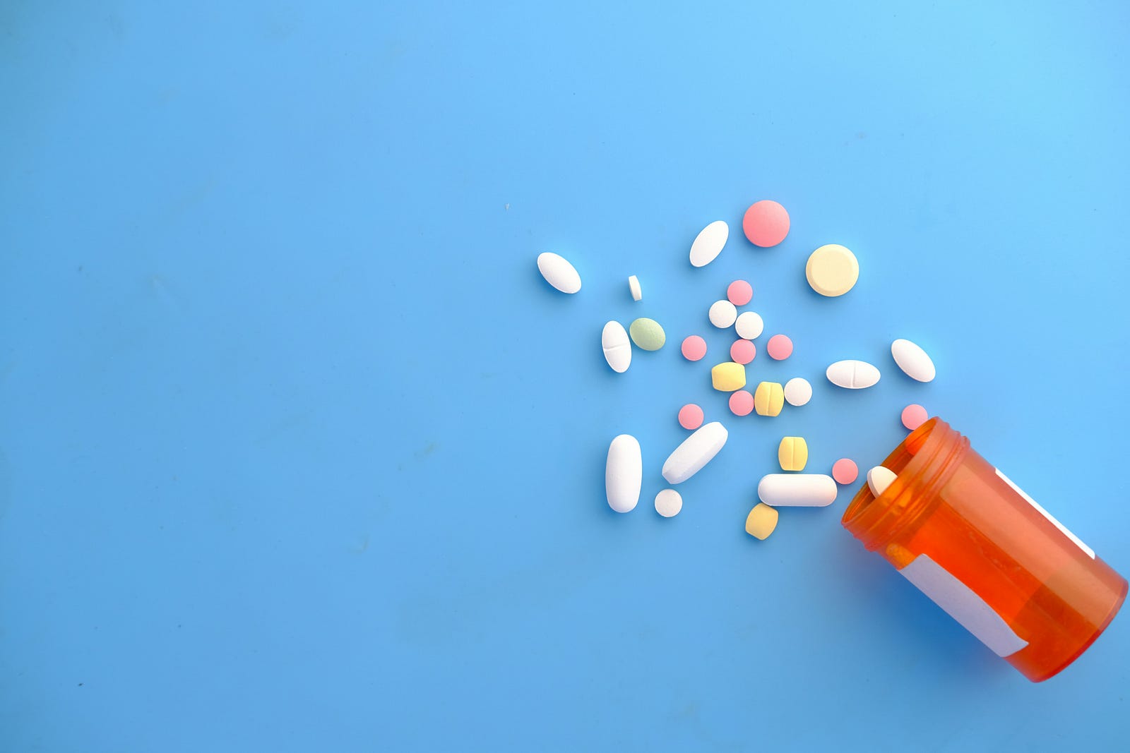 A bottle lies on its side, with pills of various colors spilling out. There is a light blue background.