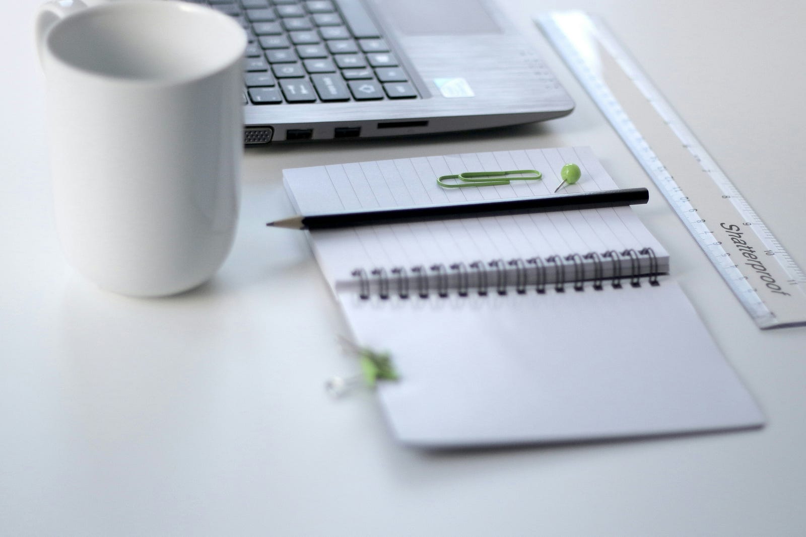 A coffee cup sits in front of a notebook and a desktop computer keyboard.