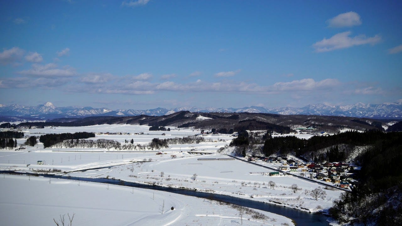 A snowy landscape with Kamuro mountains in the distance and Sakegawa river cutting across rice fields