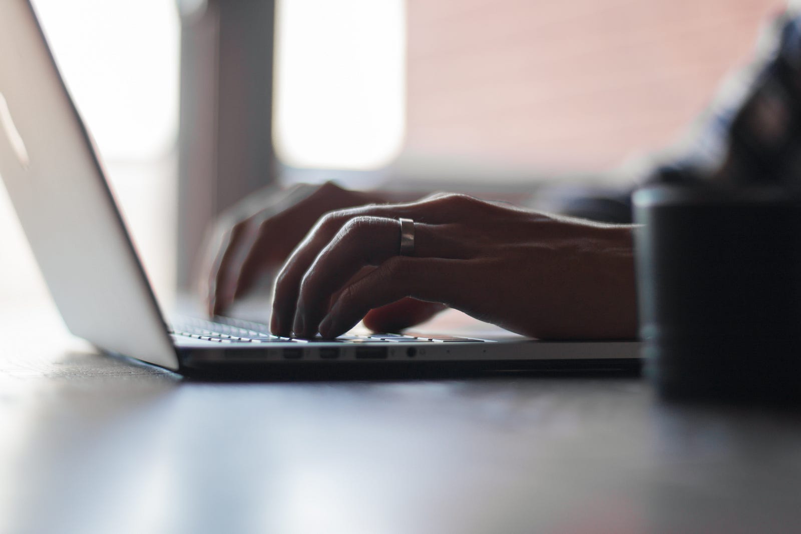 A woman’s two hands extend to type on a Apple laptop. Prolonged sitting is associated with chronic illnesses and premature mortality.