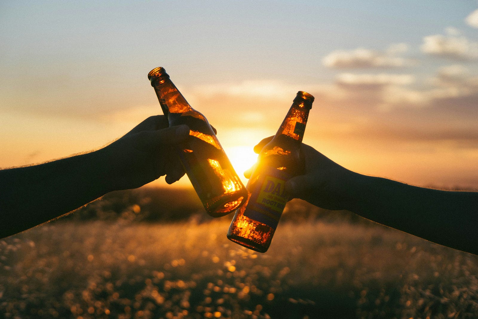 An arm from the left (and one from the right) clink bottles of beer together. Excessive alcohol shortens life length.