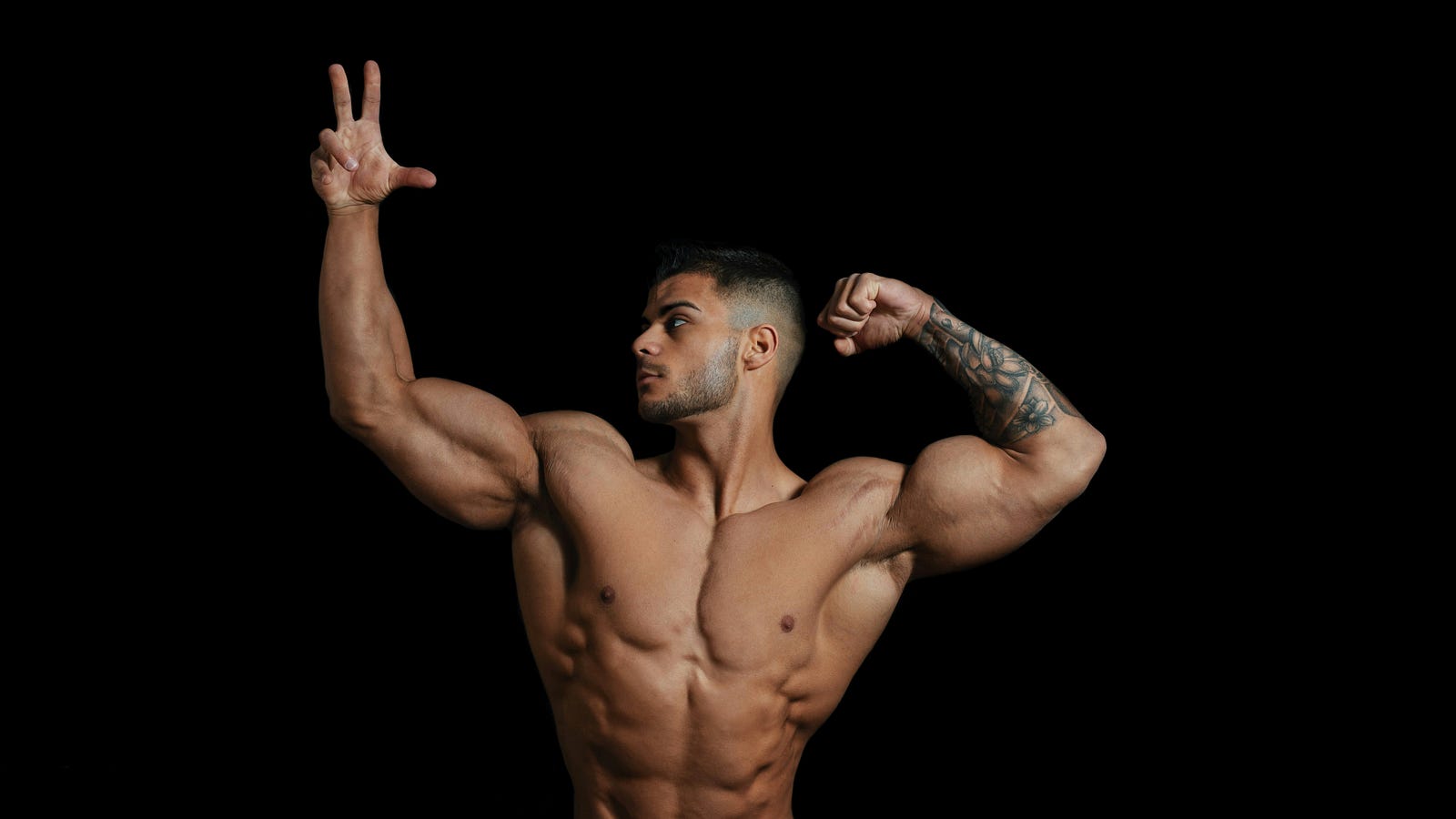 A young man poses in a body builder “hero” position.