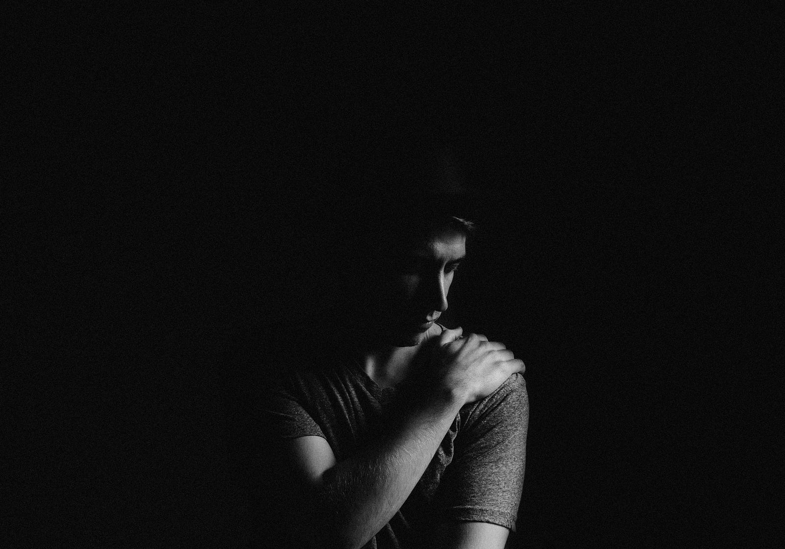 A balck and white image of a young man touching his left shoulder with his right hand.