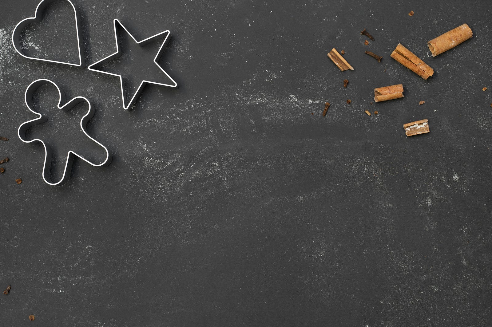 Five pieces of cinnamon on the upper right of the image, with some cookie cutout shapes to the upper left.