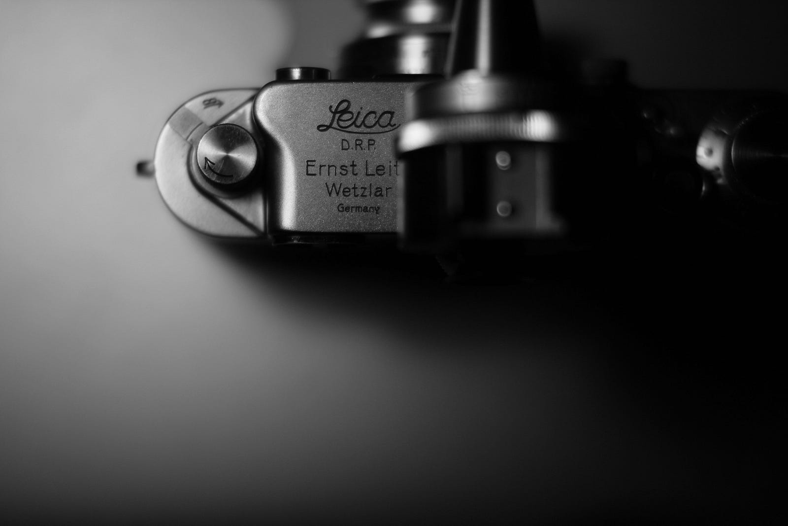 A black and white image of an old, film-based Leica camera (as seen from above). Photography adds a creative element to my experience, allowing me to preserve memories, share my adventures with others, and see the world through a new lens as I take my walk.