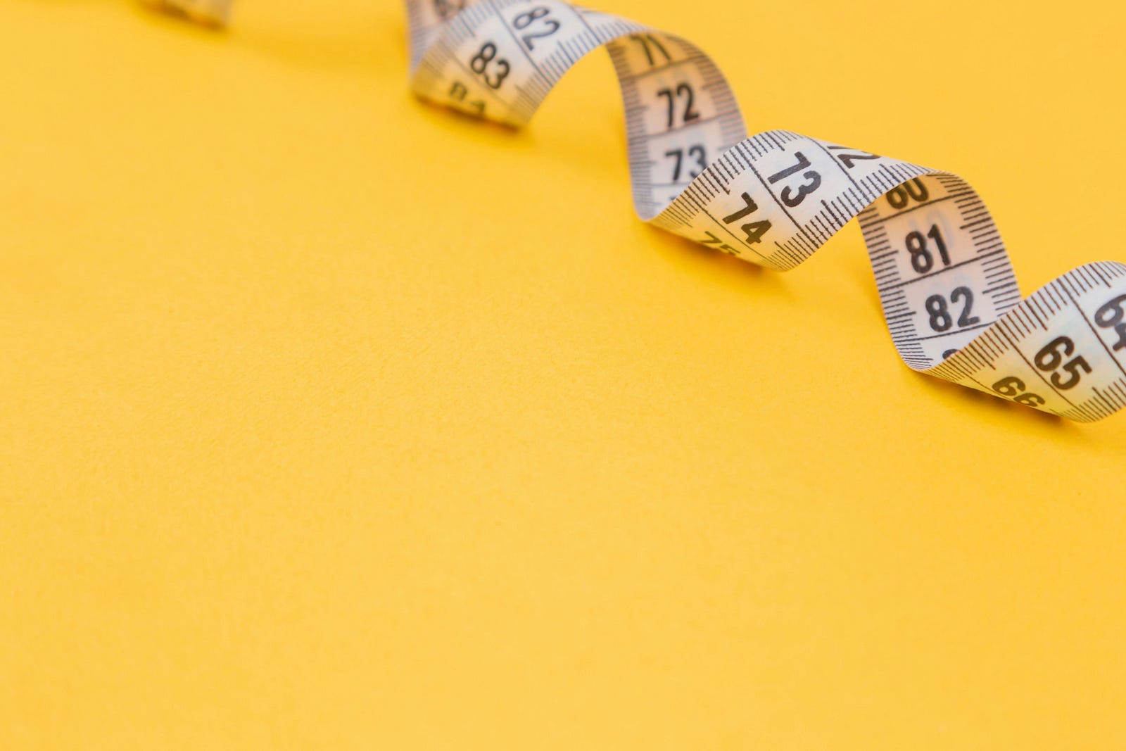 A curling cloth tape measure against a yellow background.