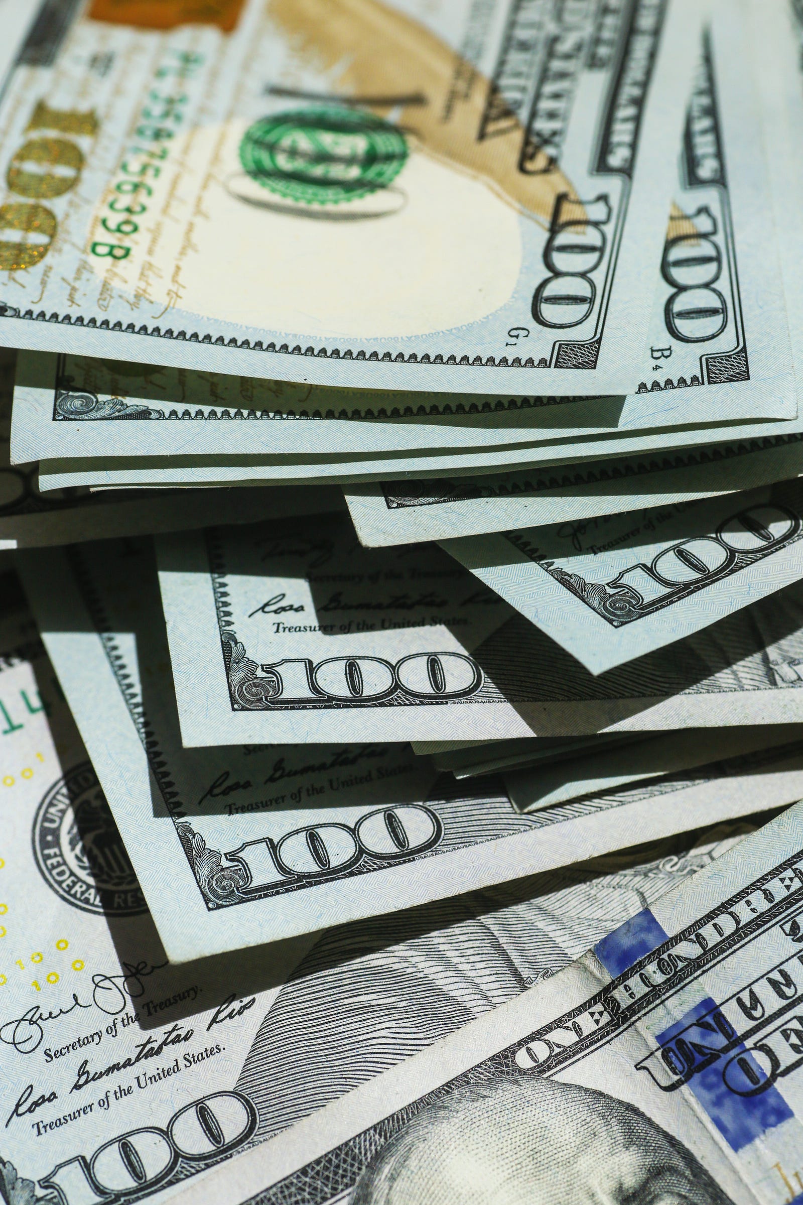 A small pile of American $100 bills (in closeup). Running indoors comes with costs (such as a treadmill purchase or joining a gym).