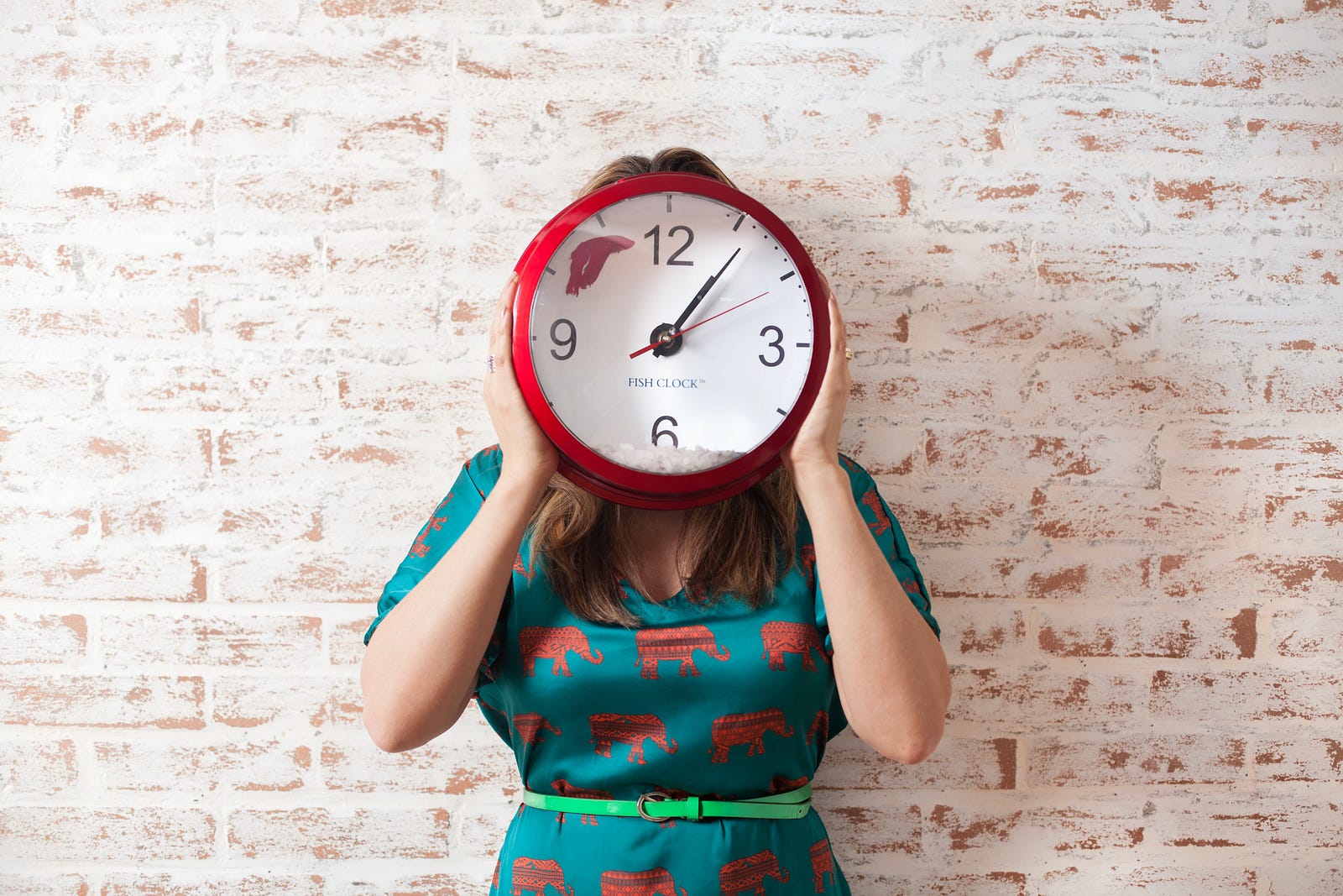 A woman holds a large red-rimmed clock (with a white face) in front of her head. She wears a simple dress and stands against a white brick wall. Disruption of circadian physiology could result in gastroesophageal reflux disease (GERD), the most important risk factor for esophagus adenocarcinoma, via altering the expression of circadian-clock genes in esophagus tissue or reducing the expression of melatonin.