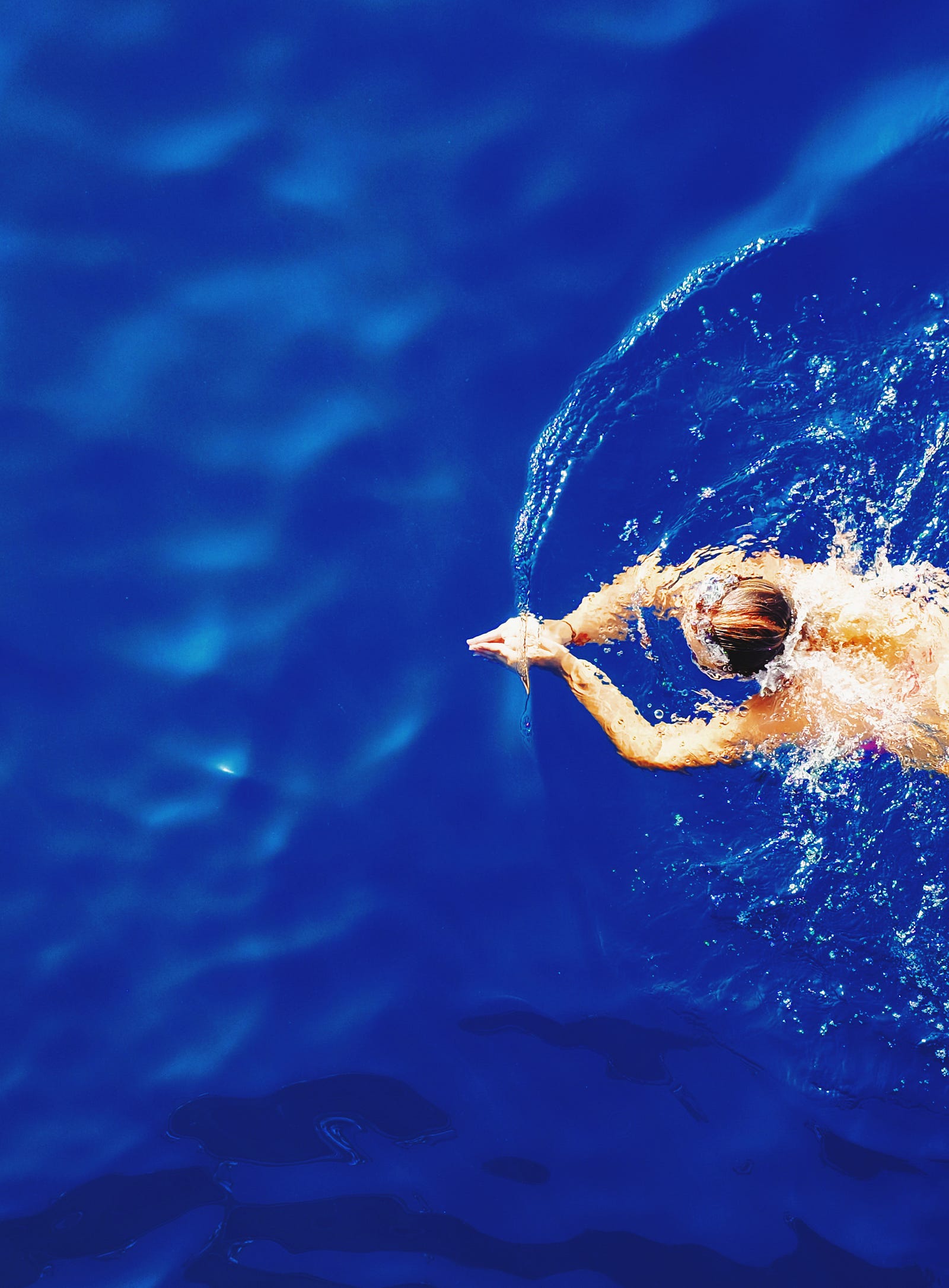 A person swims from right to left. Low-intensity exercises encompass physical activities performed comfortably, allowing individuals to maintain a steady heart rate of approximately 50 percent of their maximum rate.