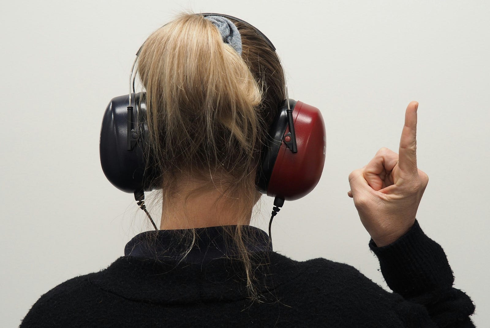 A person wears earmuffs as they raise their right arm to extend an index finger upwards.