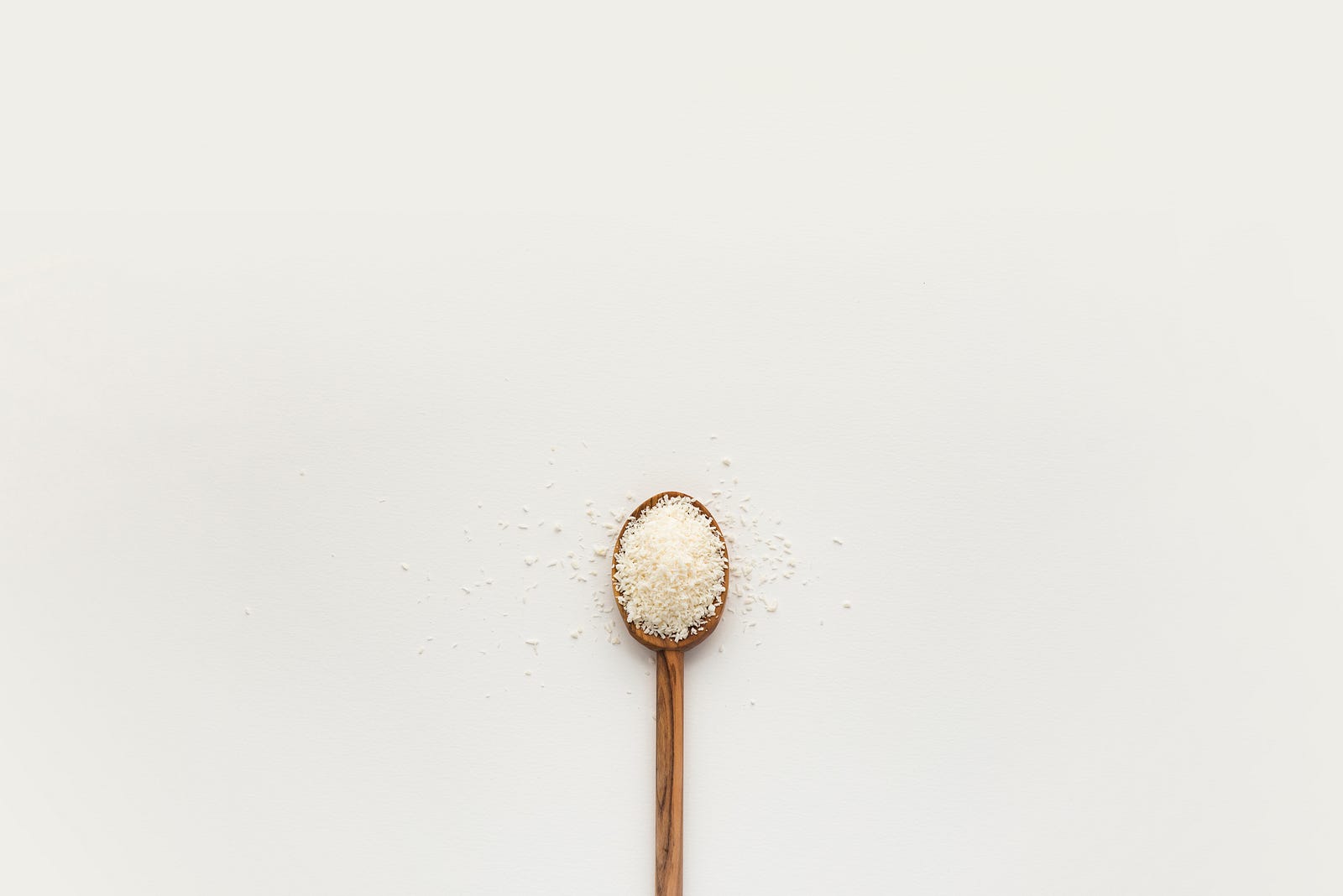 A wooden spoon extends from the bottom of the image, filled with coarse white salt. There is a white background. Too much (or too little) salt is bad for health.