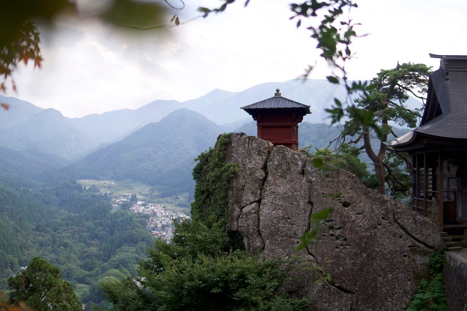A small mountain shrine at the edge of a precarious cliff with small town in the distance at Yamadera in Yamagata Prefecture, a short way away from Zao-san.