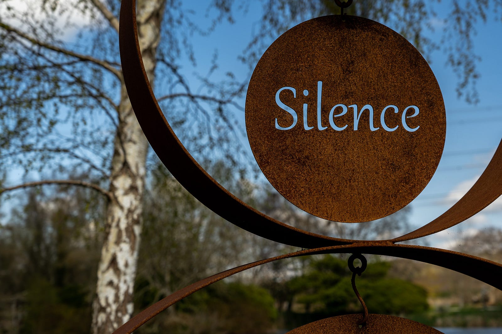 A photo of woods in the background with a red spherical sigh in the foreground reading “silence.” “Silent walking” was first coined by “Okay Sis” podcaster Mady Maio, 29, from Los Angeles, in June 2023. She is a TikTok creator.