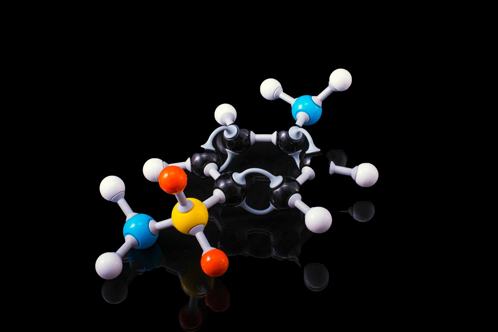 Plastic model of a molecule, multicolored against a black background. Chemogenetics inverts traditional drug discovery. Historically, scientists developed to target receptors inside cells. On the other hand, chemogenetic approaches determine a clinically approved drug first (based on bioavailability, pharmacokinetics, and tolerability).