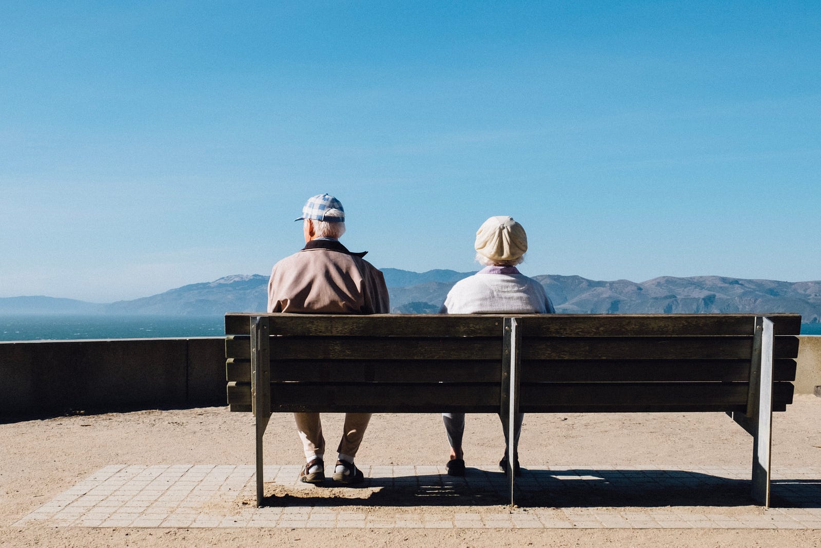 An older couple sits on a bench. We see them from behind as they look at mountains in the distance. Colorectal screening should continue until age 75, according to the U.S. Preventative Services Task Force, after which it depends on the individual patient and their doctor until age 85.
