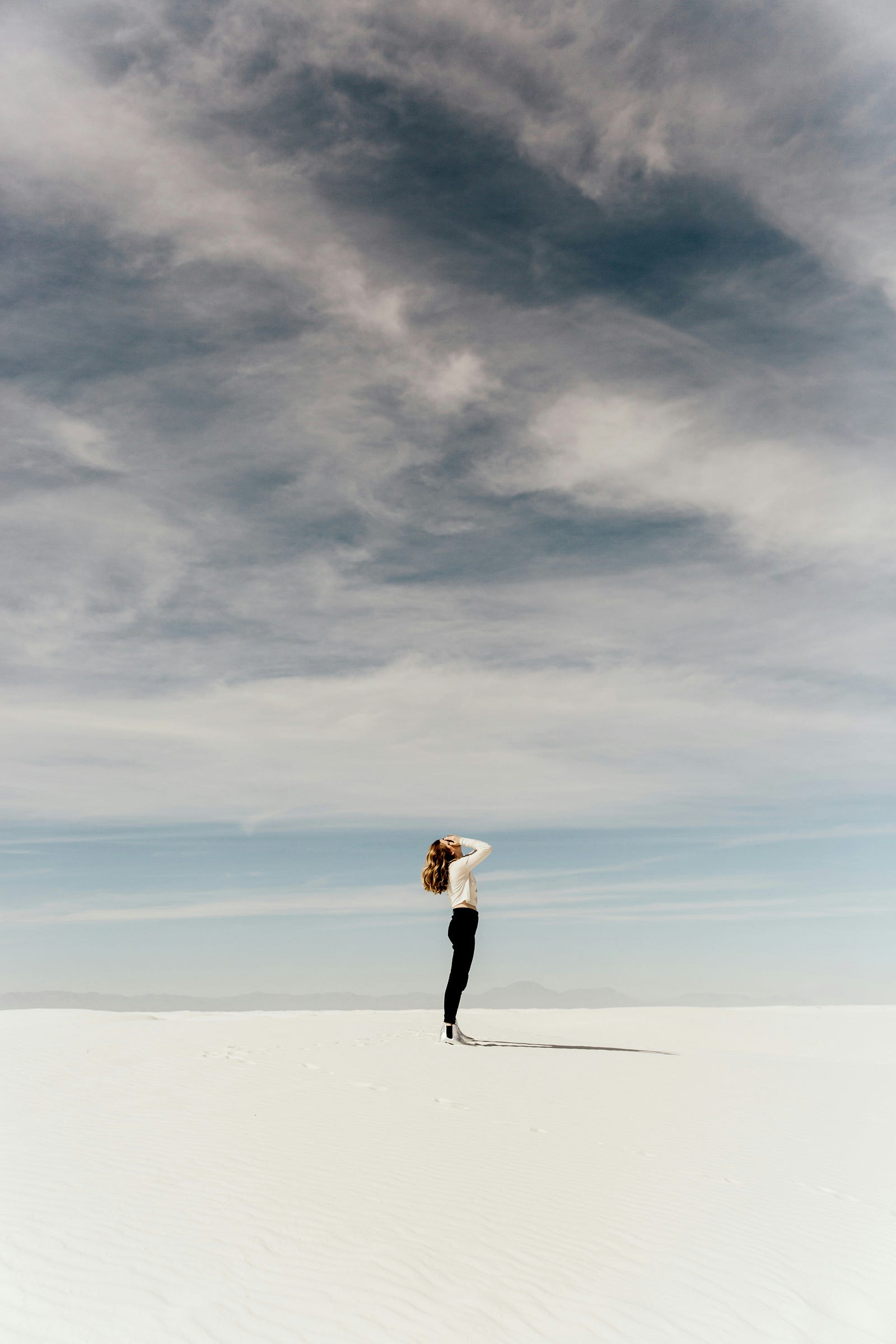 A young woman stands in profile against an open background that includes a sky filled with wispy cirrhus clouds.