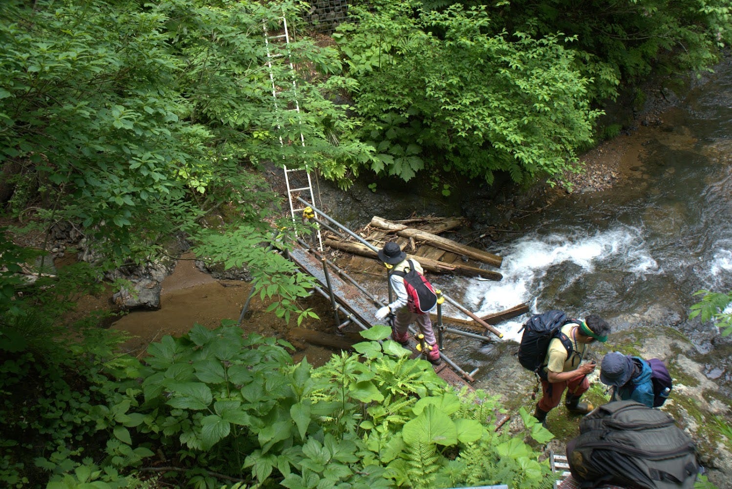 Someone walks across a bridge made of temporary metal scaffolding and ladders. The original bridge lies next to it in the river.