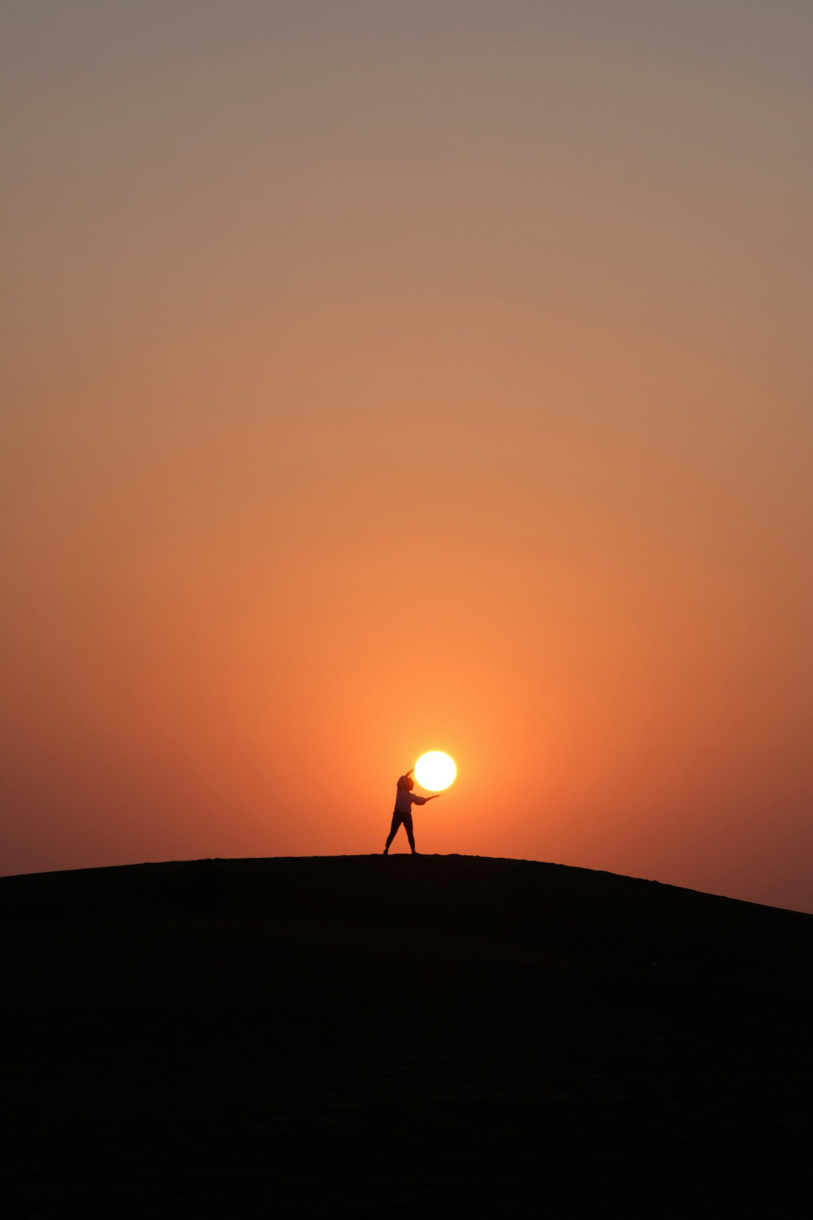 A person in the distance is in silhouette as they extend their arms to embrace the setting sun.