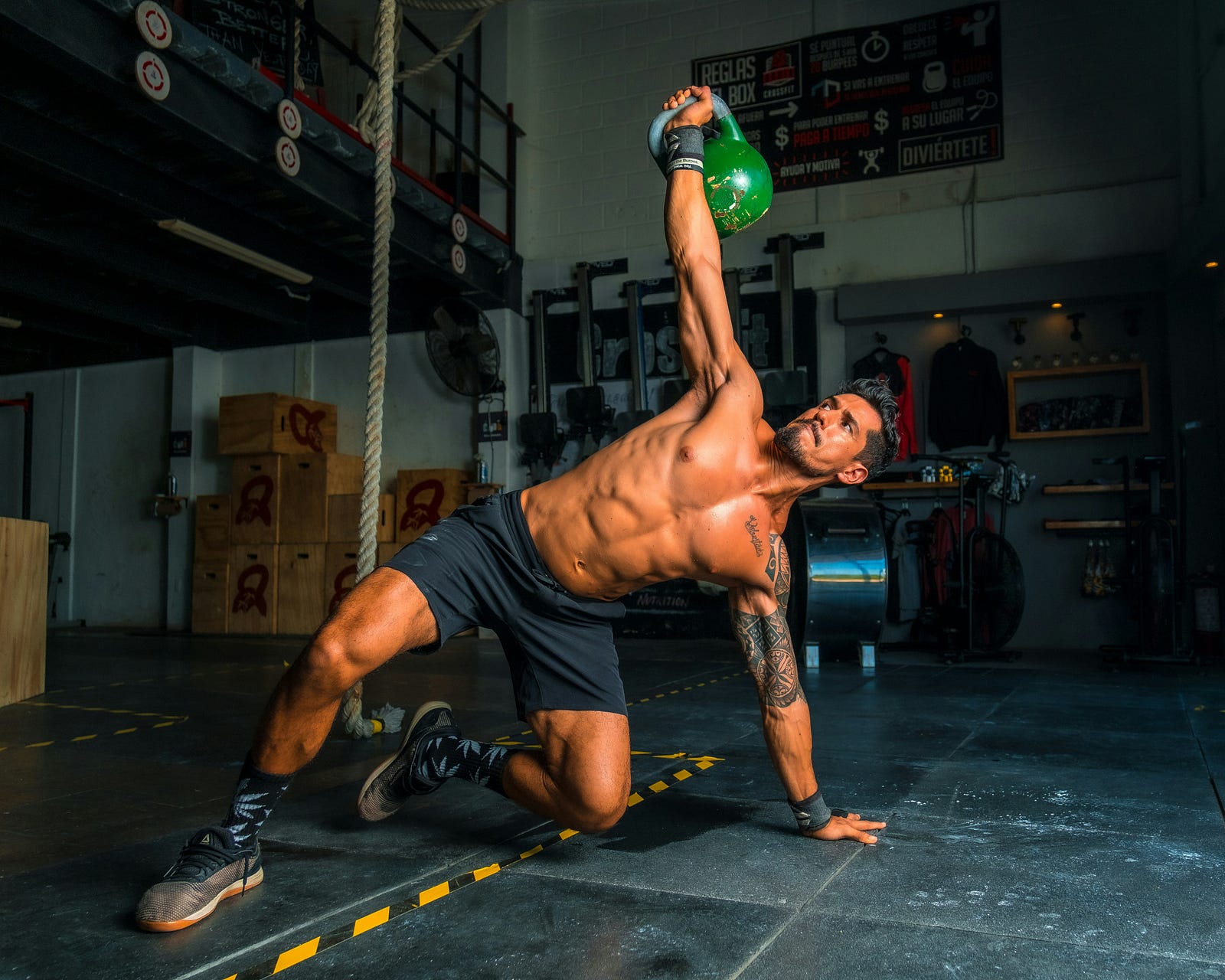 A man lifts a green kettlebell in a gym.