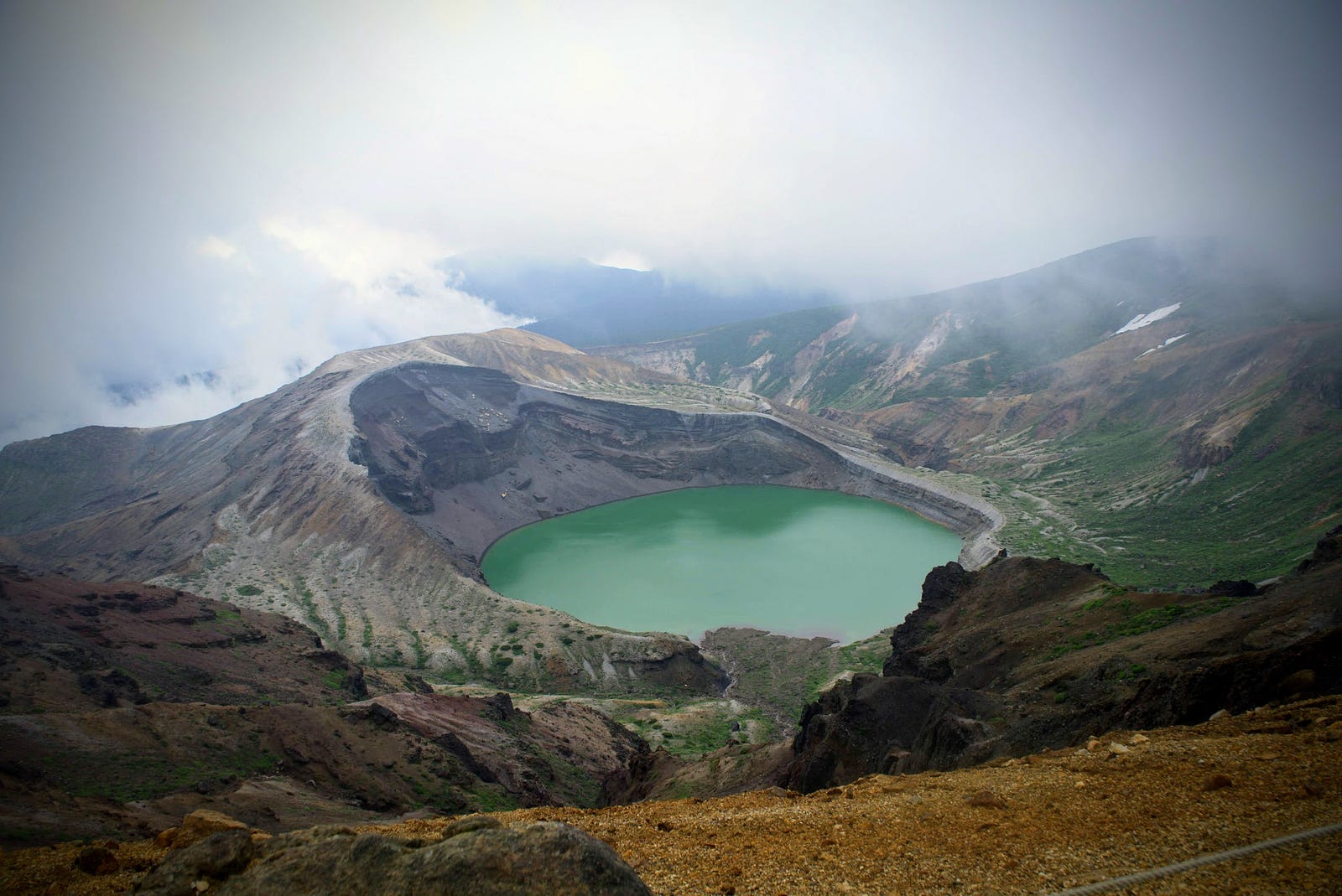 The emerald green crater lake ‘Okama’ of Zao-san surrounded by cloudy mountain peaks