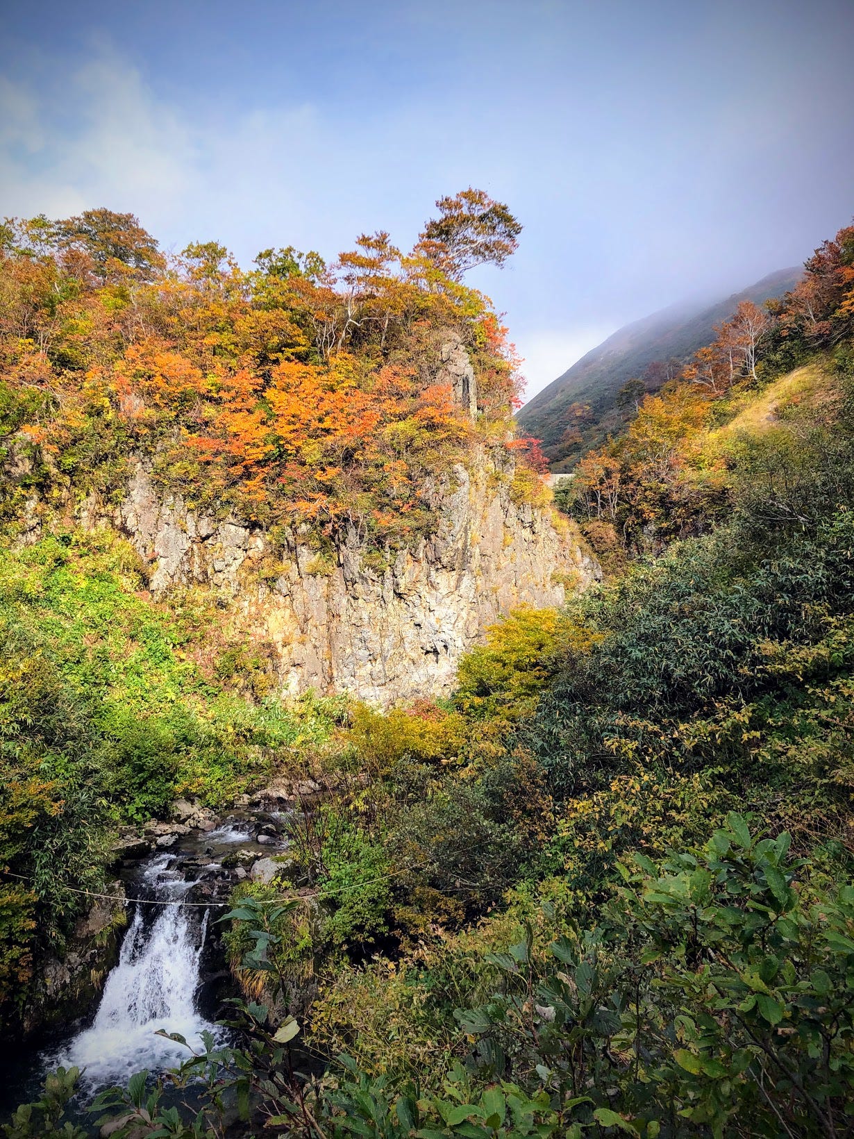 A river carves its way around a tall cliff complete with waterfall that is used for yamabushi waterfall meditation training