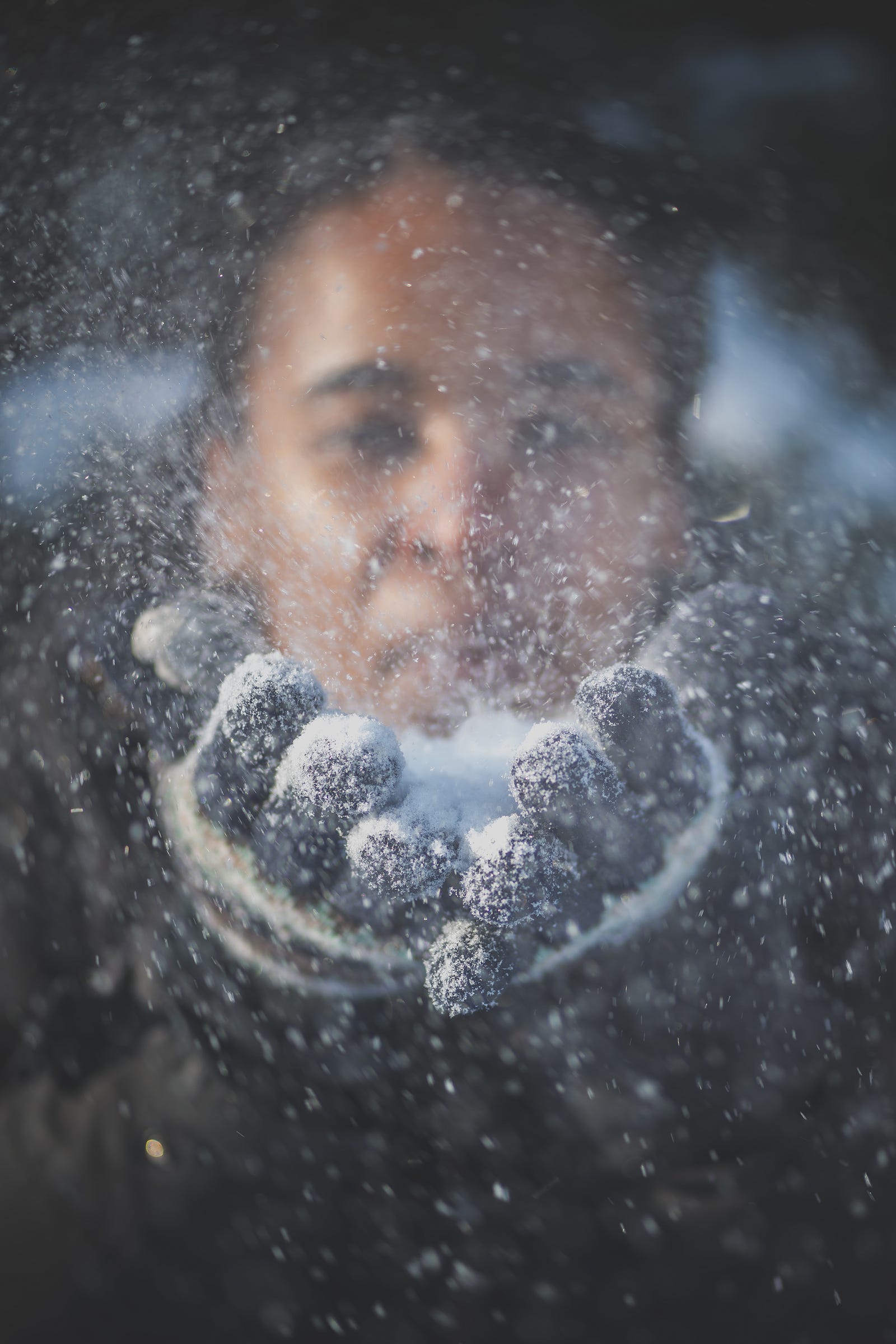 A black woman has her hands forward. She blows snow from her hands. The picture is blurry.