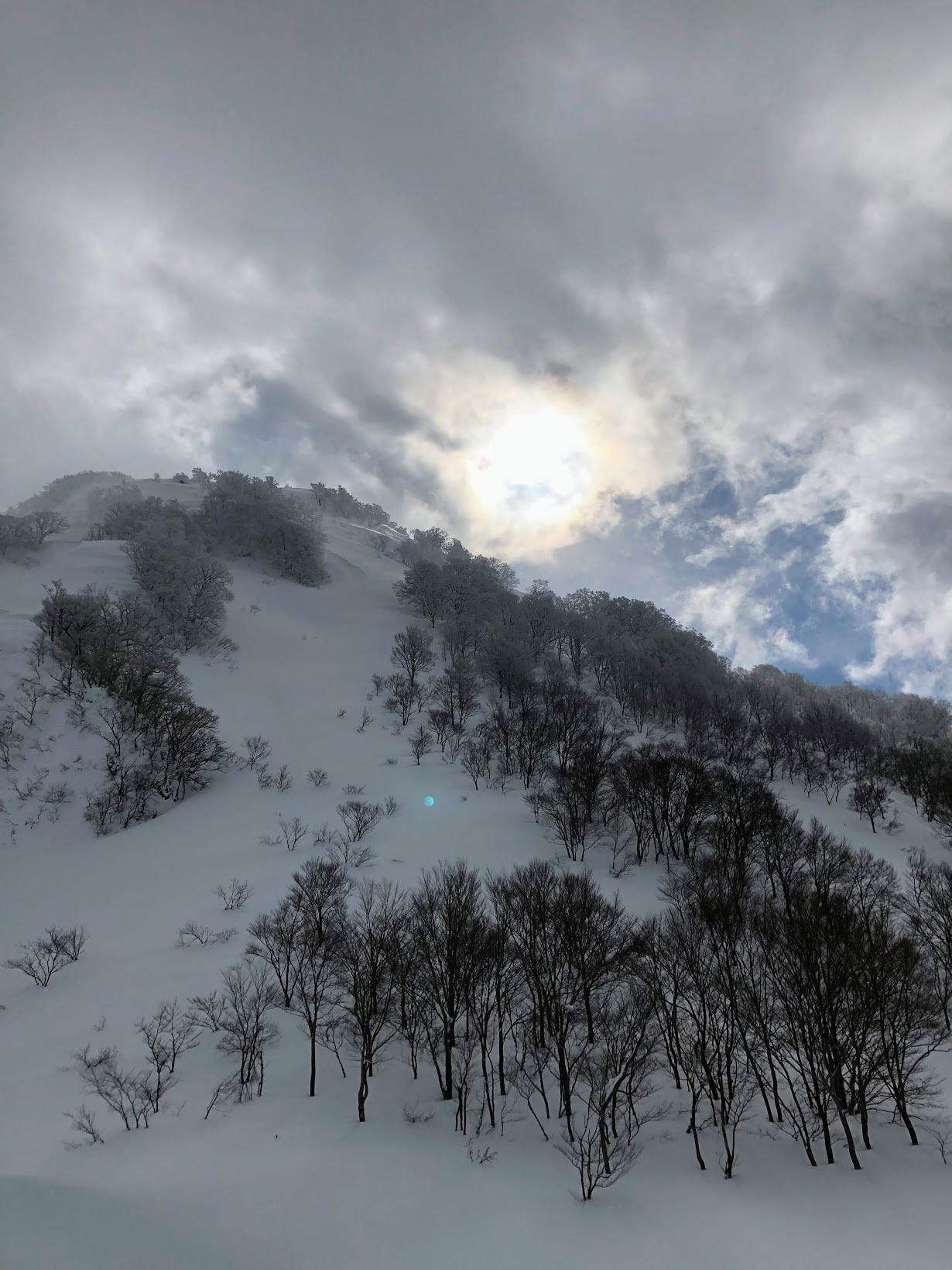 The sun basks over a snowy mountain cliff that has hidden caves on it near Mt. Yudono Shrine