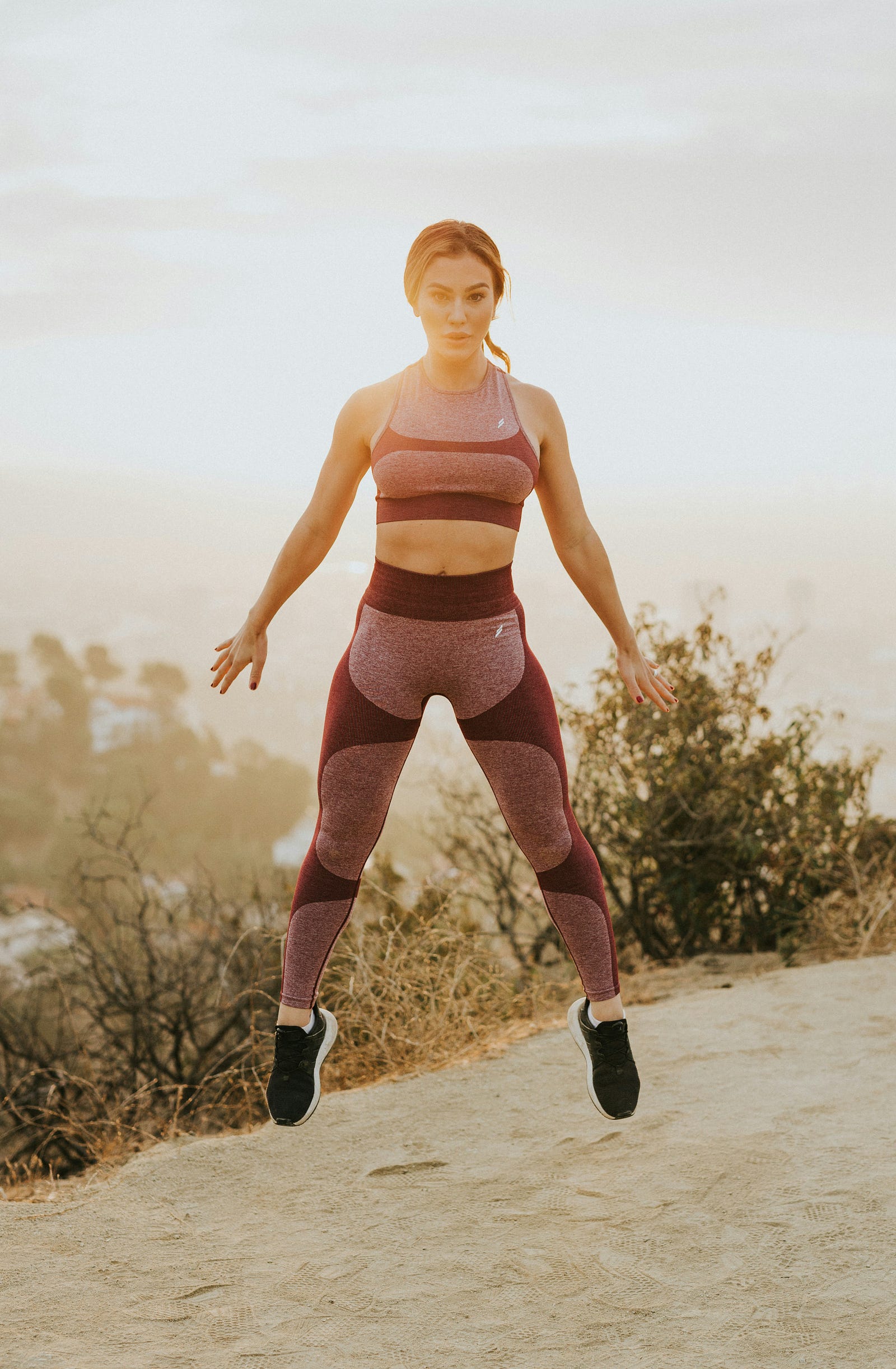 A young woman jums up, her arms down and to the side and her legs forming an inverted V.