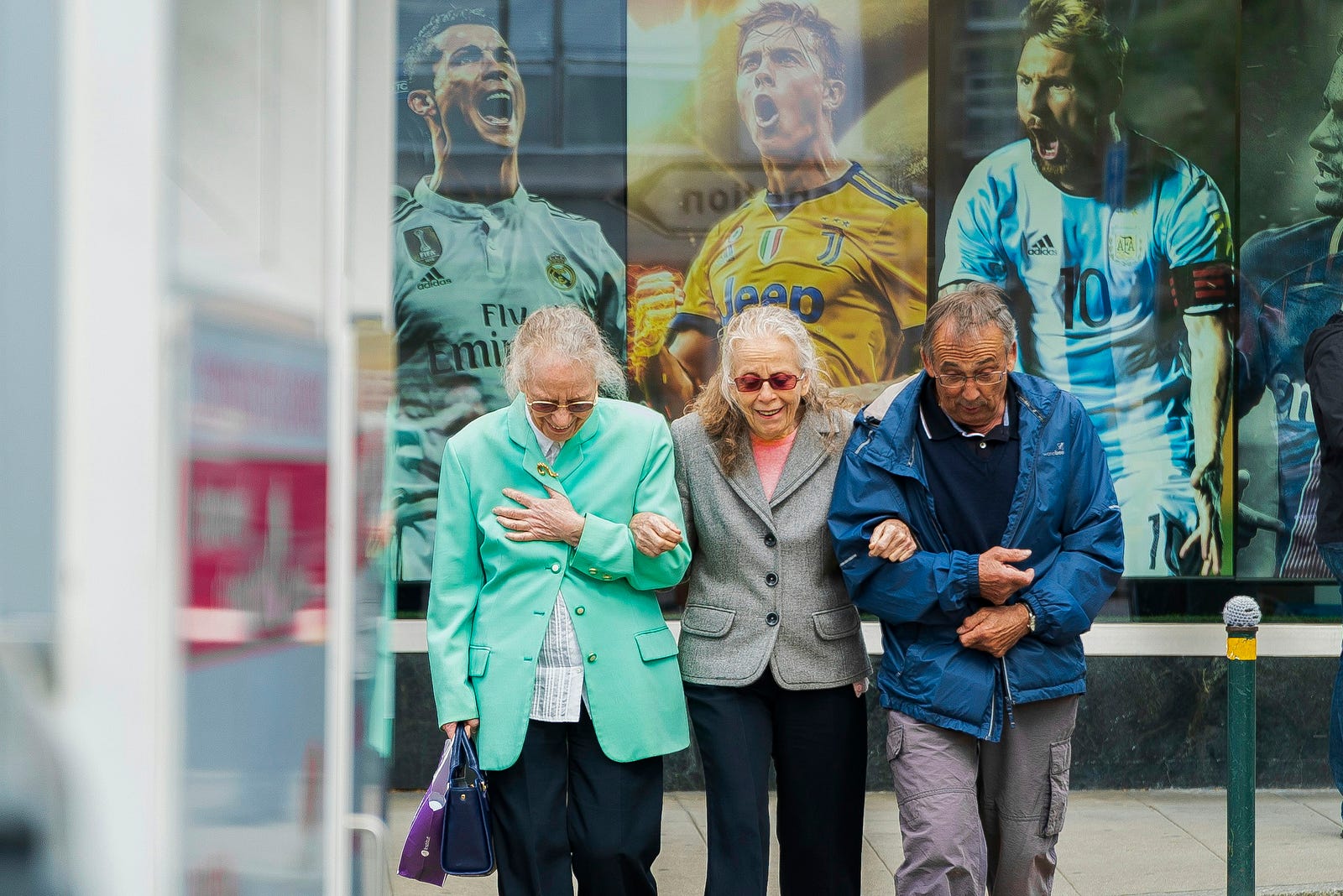 Three older individuals walk towards us, arms intertwined.