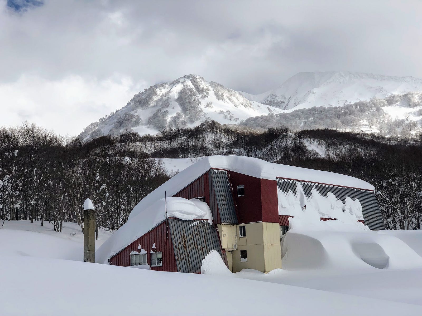 A defunct Ryokan traditional Japanese Inn inundated with snow sits in the foreground of this snowy landscape with the real Mt. Yudono in the background