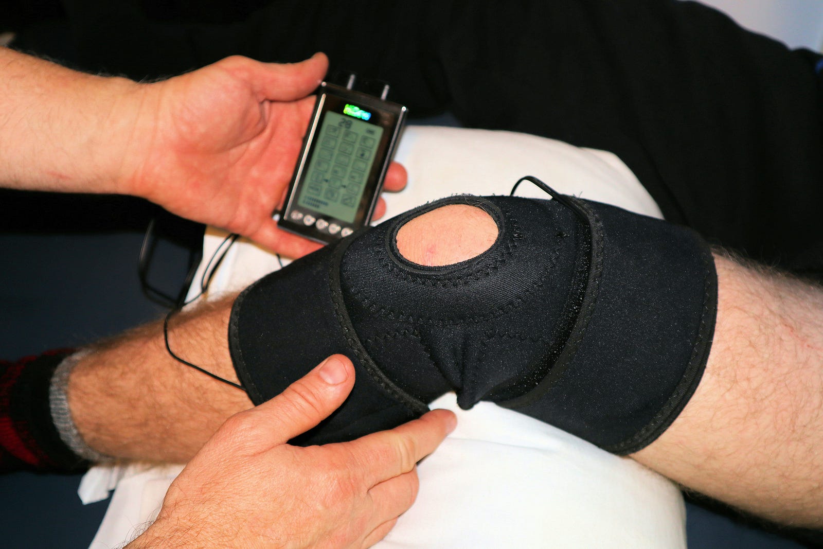 A left knee wears a brace, with an electric stimulator placed on their skin.