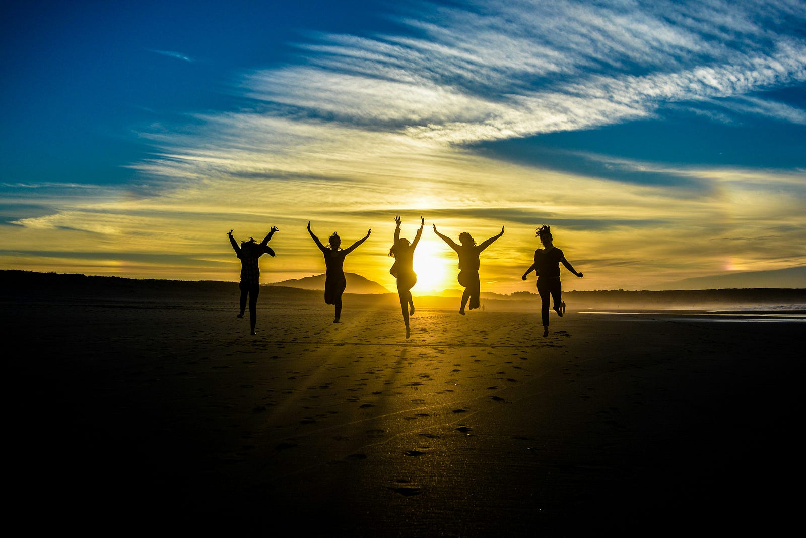 We see five people in silhouette jumping as the sun sets behind them.