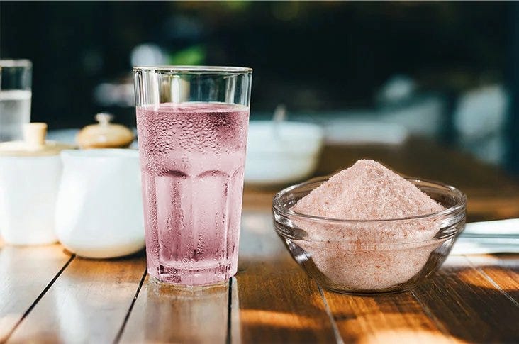 A glass of pink saltwater solution next to a bowl of Himalayan pink salt, highlighting its health benefits and uses in hydration