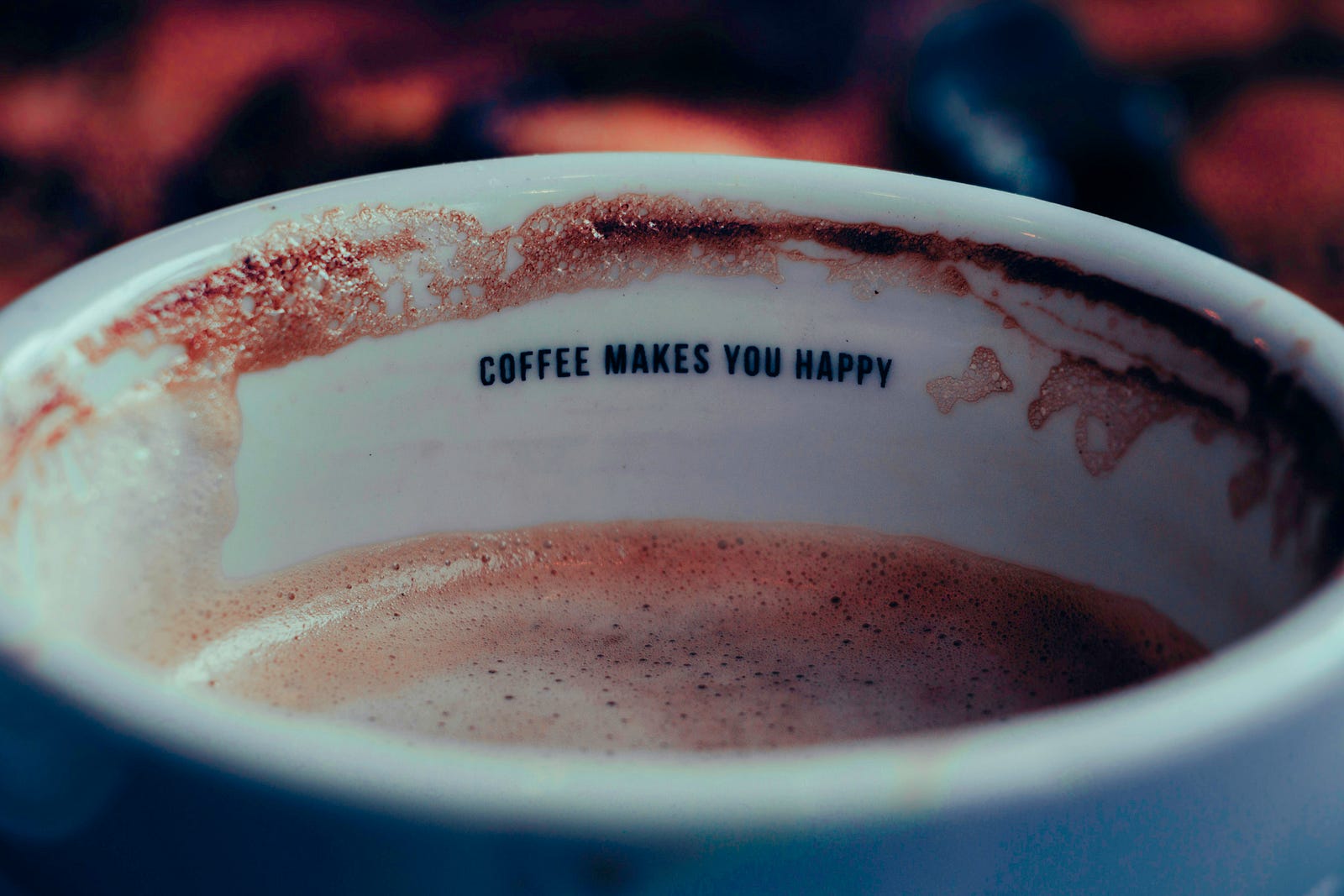 A cup with coffee, with the words “Coffee makes you happy” written on the upper inside of it.