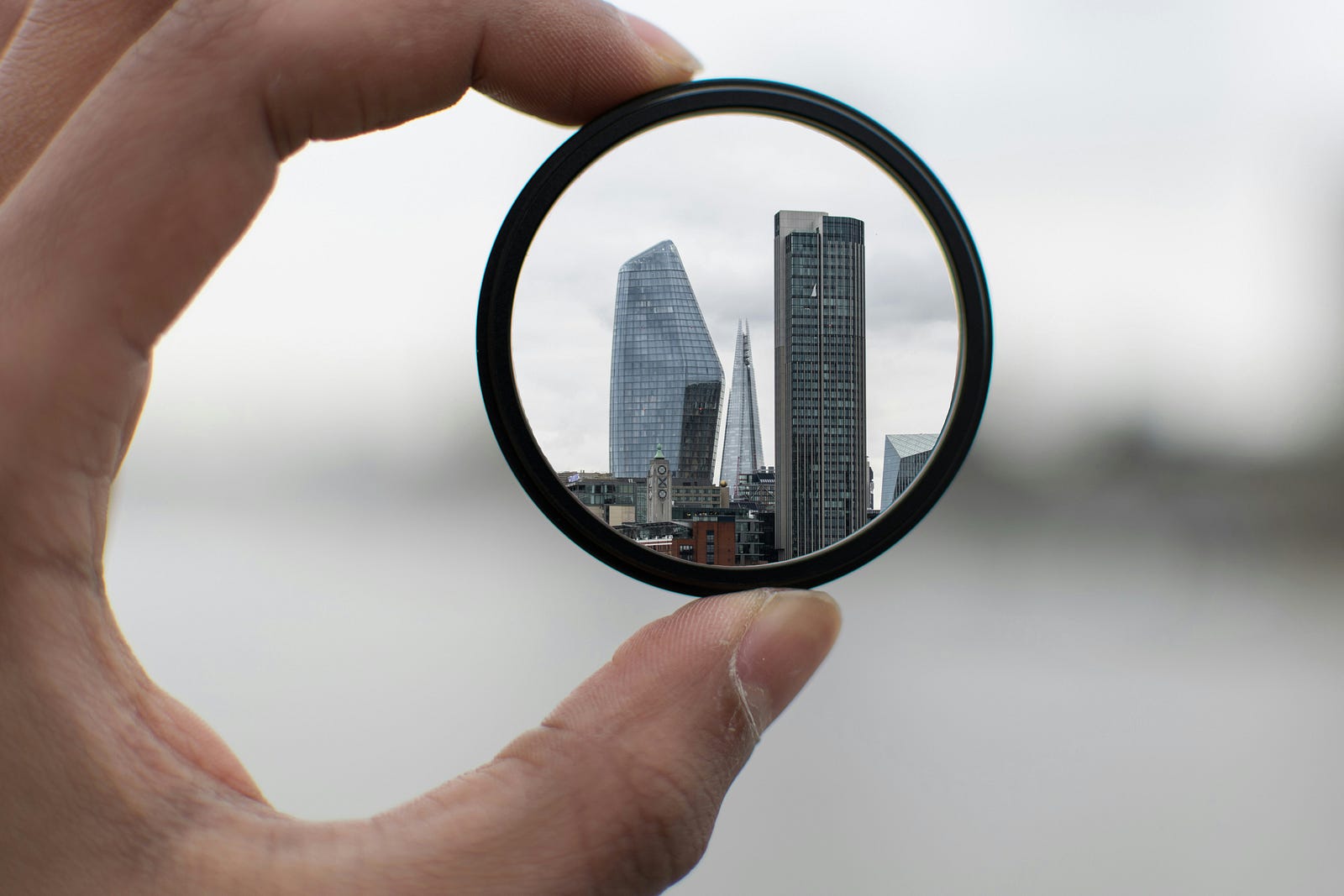 A hand holds a round balck-rimmed glass. We see buildings in the distance.