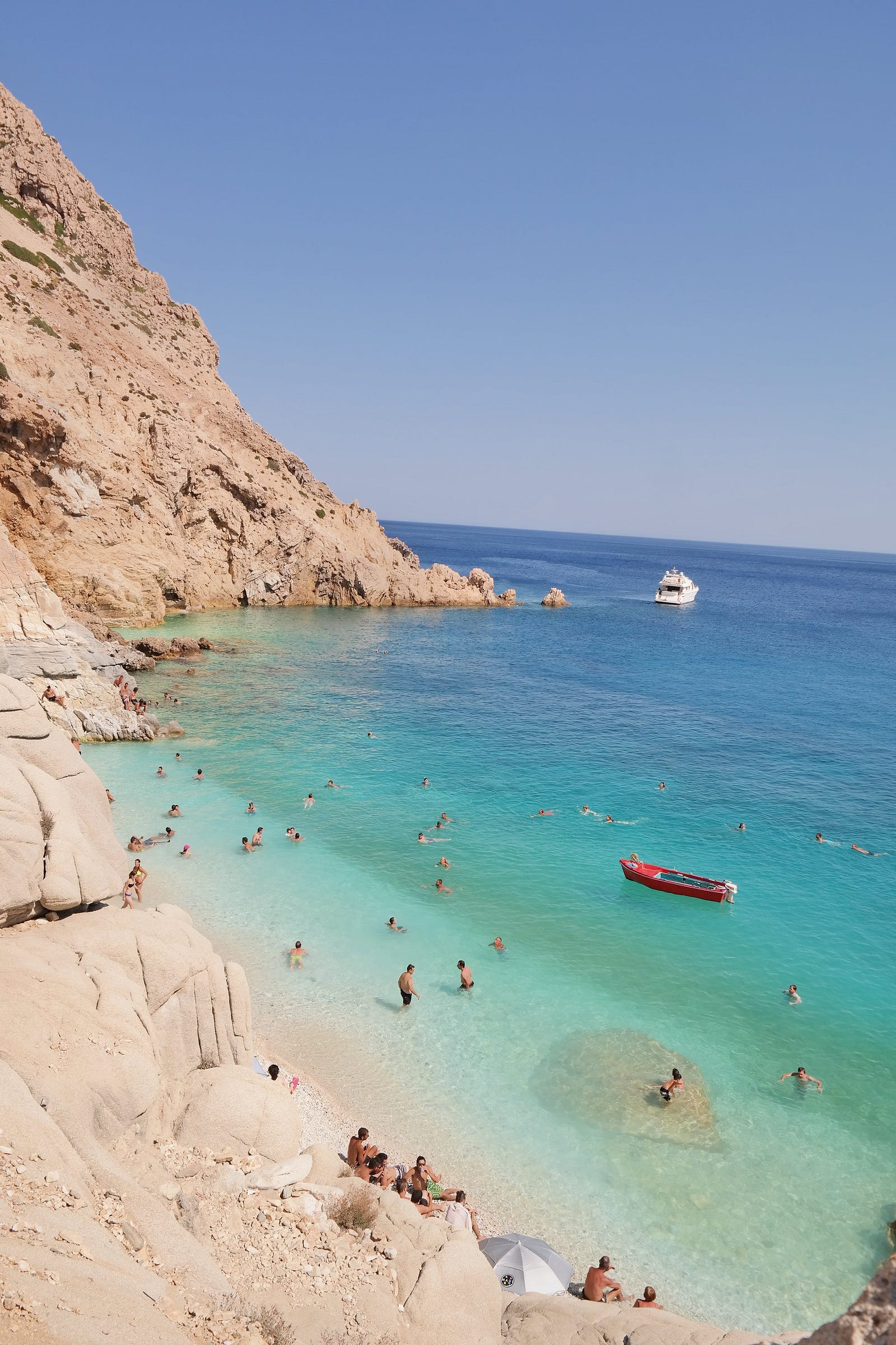 Blue-green water of the sea comes up against sand-colored cliffs in Ikaria (Greece). Blue zone habits can extend lifespan and health span.