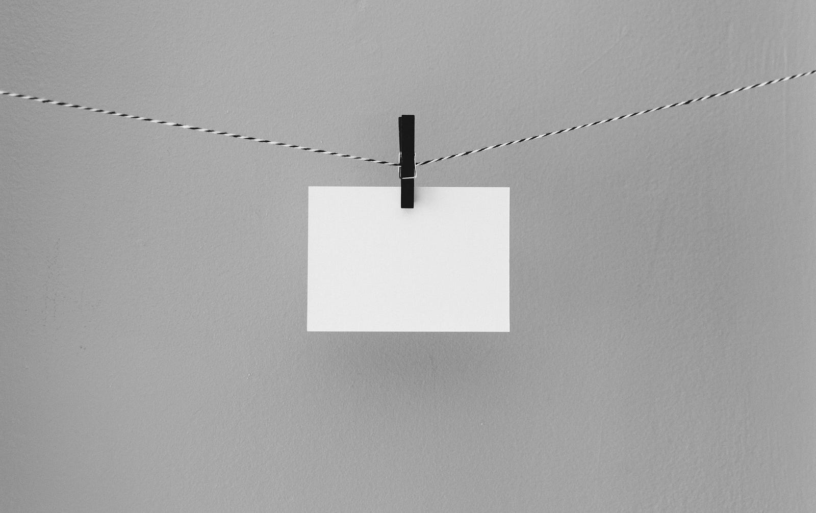 A blank small rectangular paper hangs by a clothespin from a string.