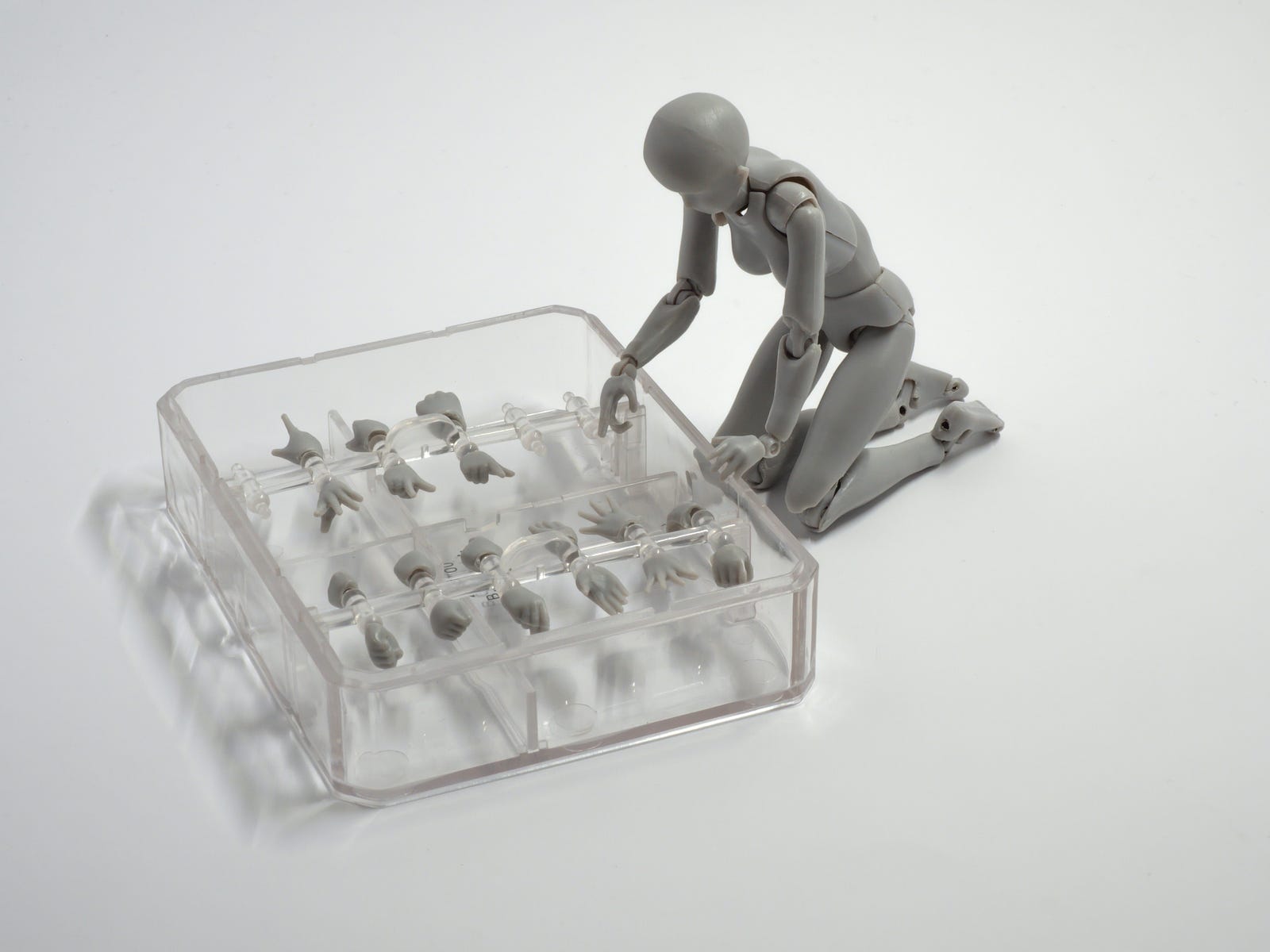 A toy figurine looks at a clear box, with sections each containing a body part that can snap into the figurine.