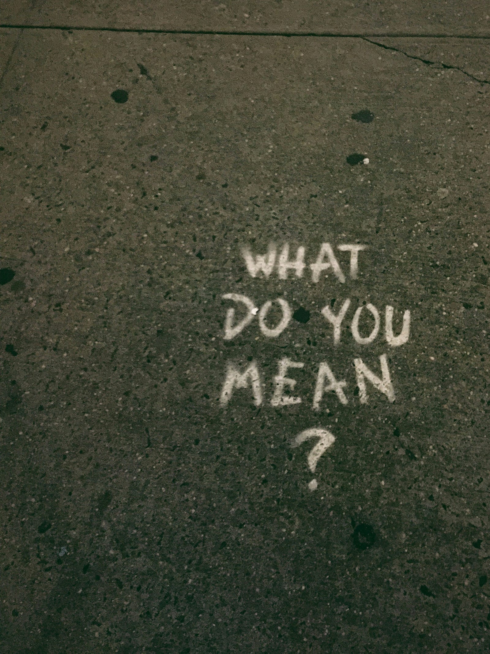 “WHAT DO YOU MEAN?” written in chalck on black asphalt.