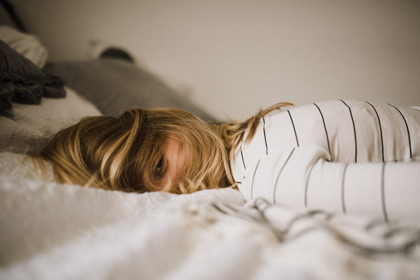 A blonde woman lies on her right side, her head flat against the bed. Regular napping is linked to higher risks for high blood pressure (hypertension) and stroke.