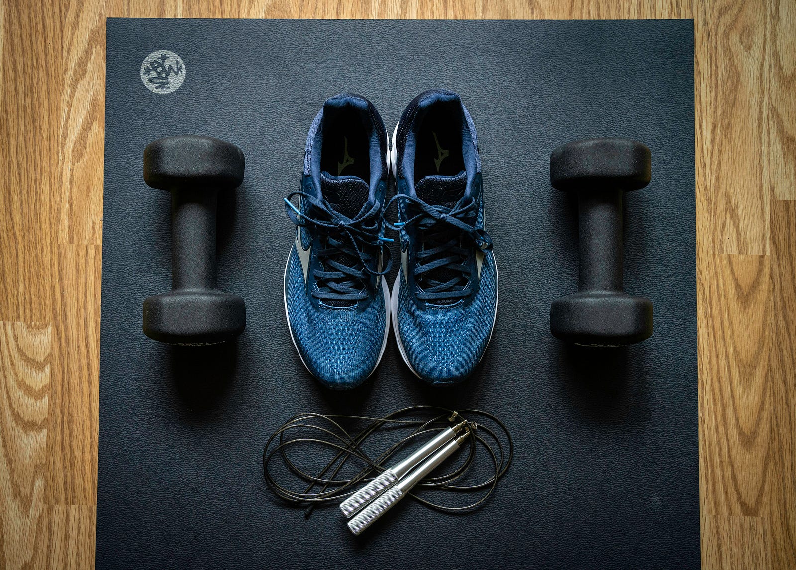 Two blue sneakers, flanked by small dumbbells. A jumprope is in the foreground. The photo is from above.